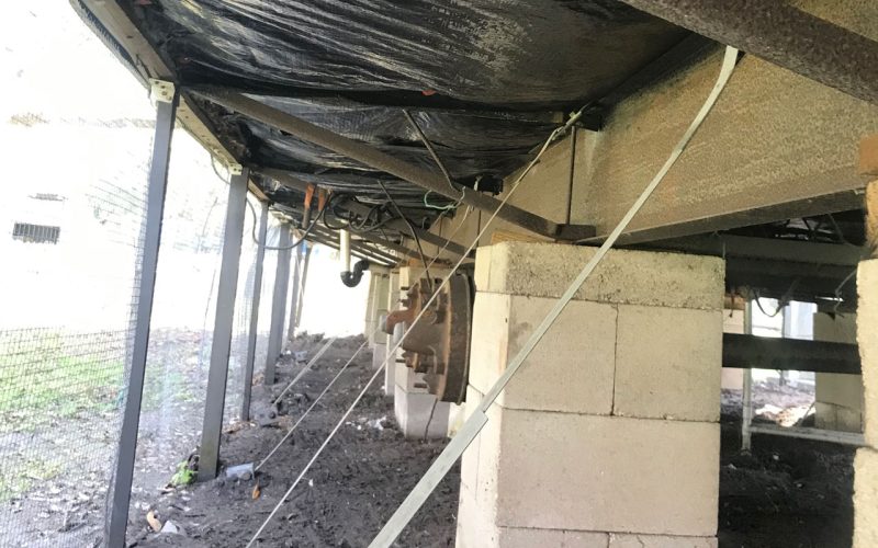 Mobile home crawl space with vapor barrier and tie-down straps being installed mid-project