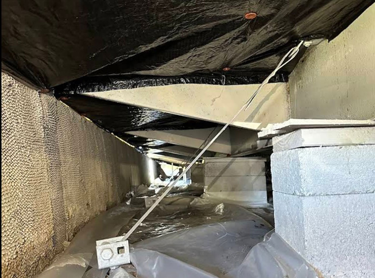 Tie-down strap tensioned from the frame of a home to its ground anchor beside a block pier