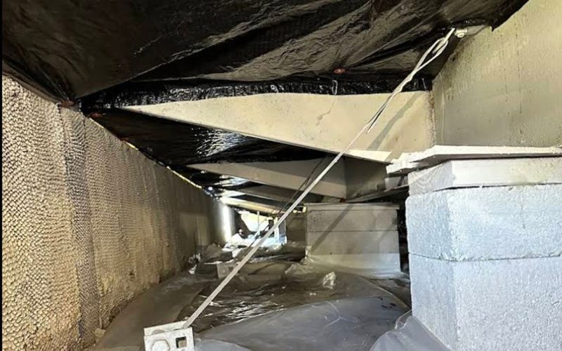 Galvanized mobile home tie-down straps anchored to concrete piers in a manufactured home crawl space