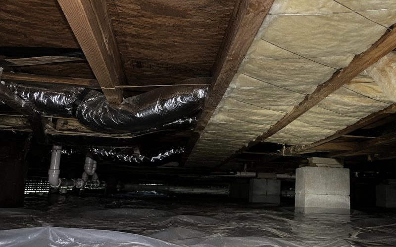 New insulation fitted between the floor joists under a home, with ductwork and bare subfloor still open alongside